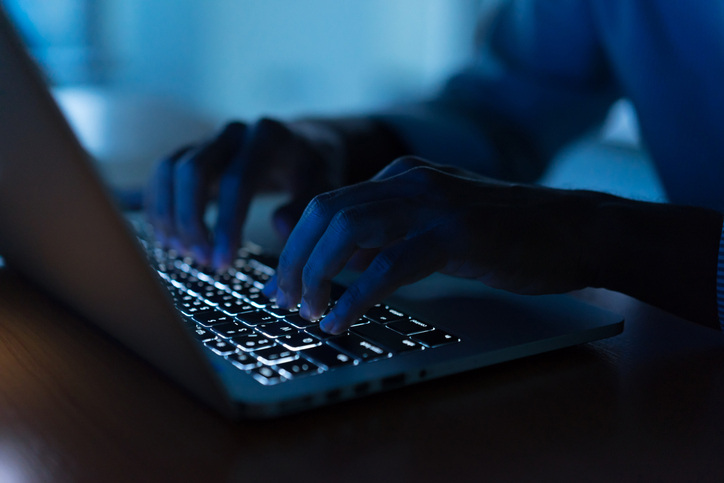 person typing on lit-up laptop keyboard in dark room