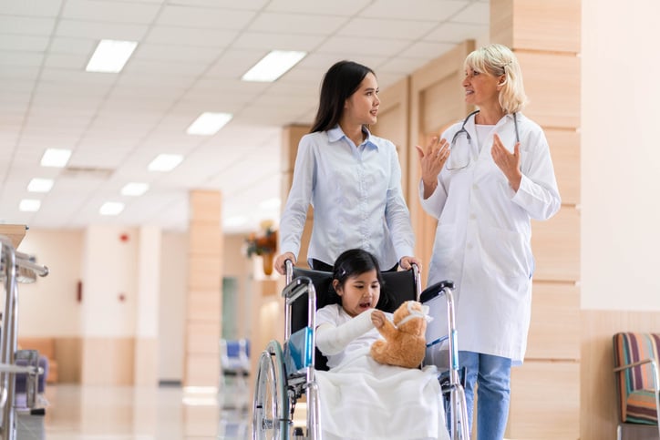 child in wheelchair and their mother walking with doctor at hospital